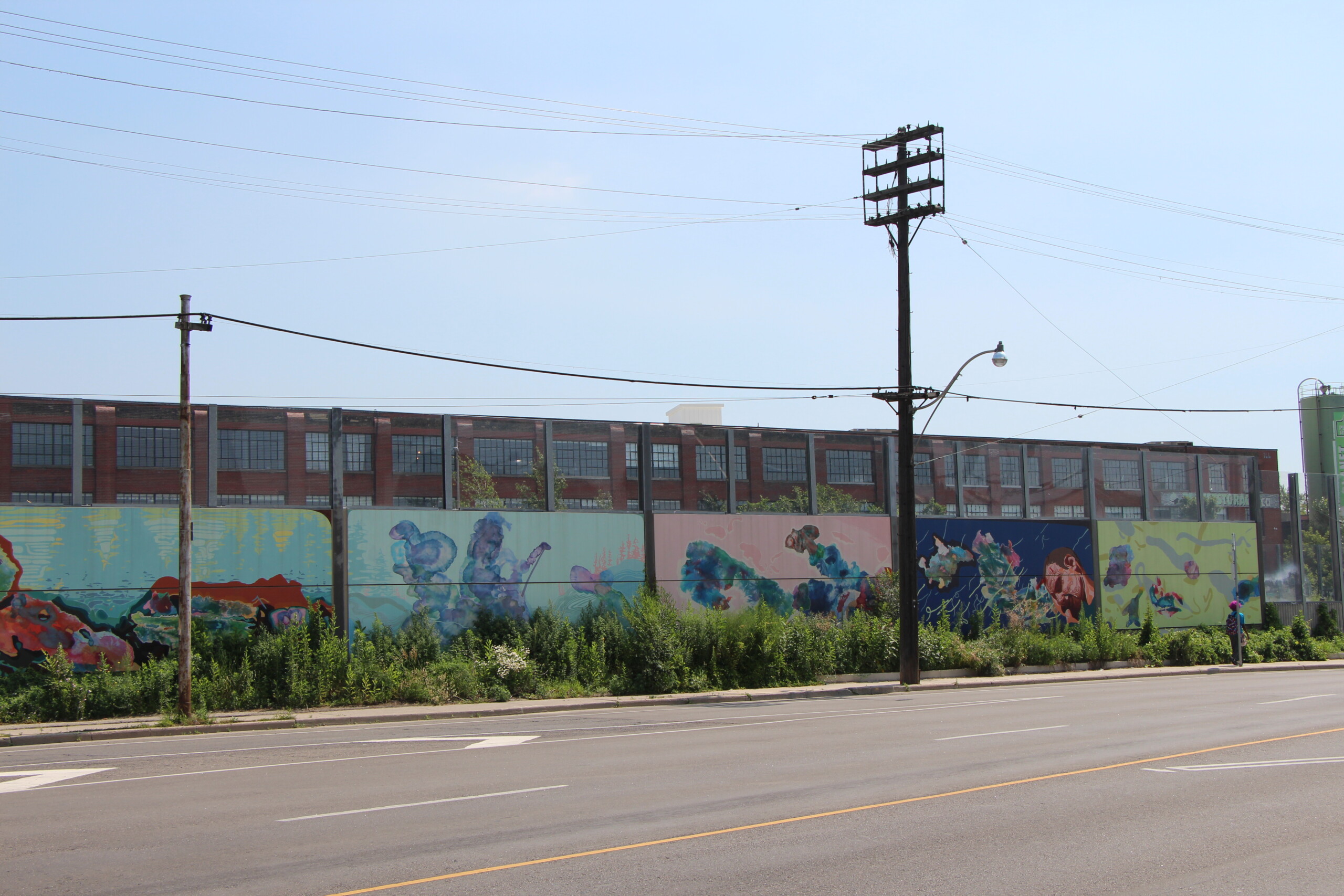 Plain concrete noise barrier panels featuring murals painted by local artists along Metrolinx's Union Pearson Express rail line in Toronto, ON.