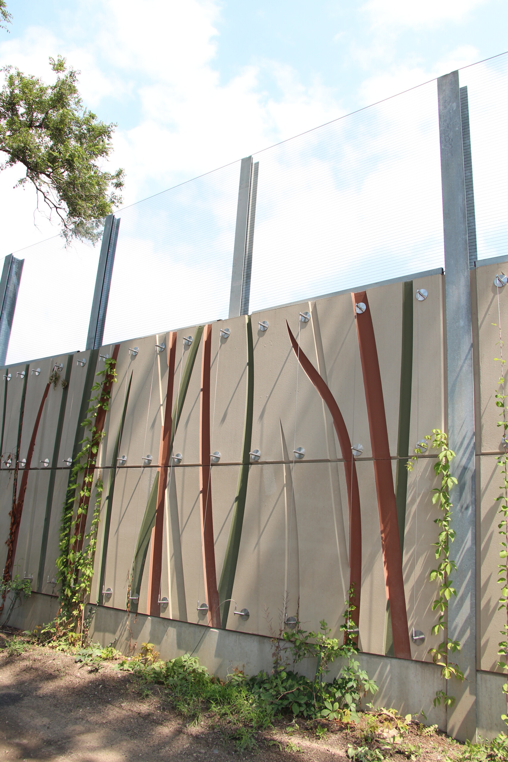 Noise barrier with Durisol absorptive panels featuring a custom "grasslands" pattern topped with Transparent Acrylite Soundstop sheets along Metrolinx's Union Pearson Express rail line in Toronto, ON.