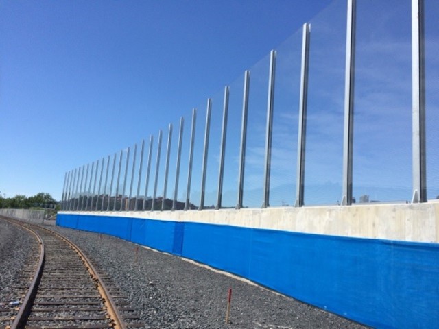 Transparent noise barrier panels with Bird Guard mounted on a concrete parapet wall along a railway track in Pointe-Saint-Charles, QC.